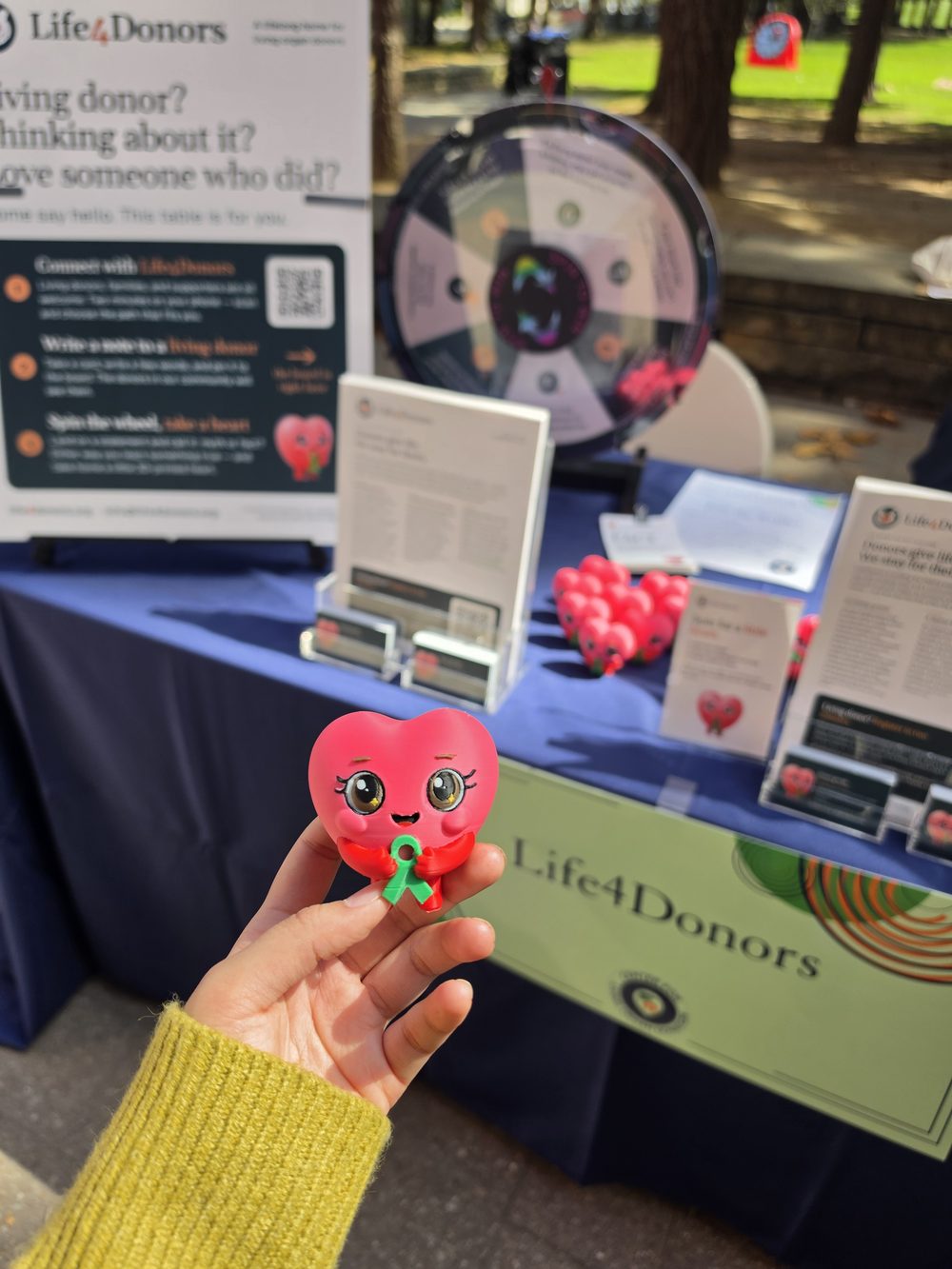A hand holds a small pink Liv keepsake with a green ribbon in front of the Life4Donors booth