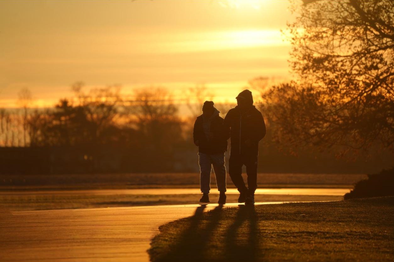 Two people walk side by side along a park path at sunrise